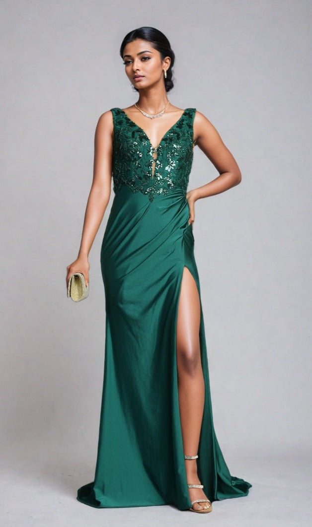 Woman in the Sequin-Bodice Long Prom Dress Chicas YG5032—an emerald green, sleeveless, sequin-detailed gown with a thigh-high slit—styled with gold heels and a clutch, poses against a plain backdrop.